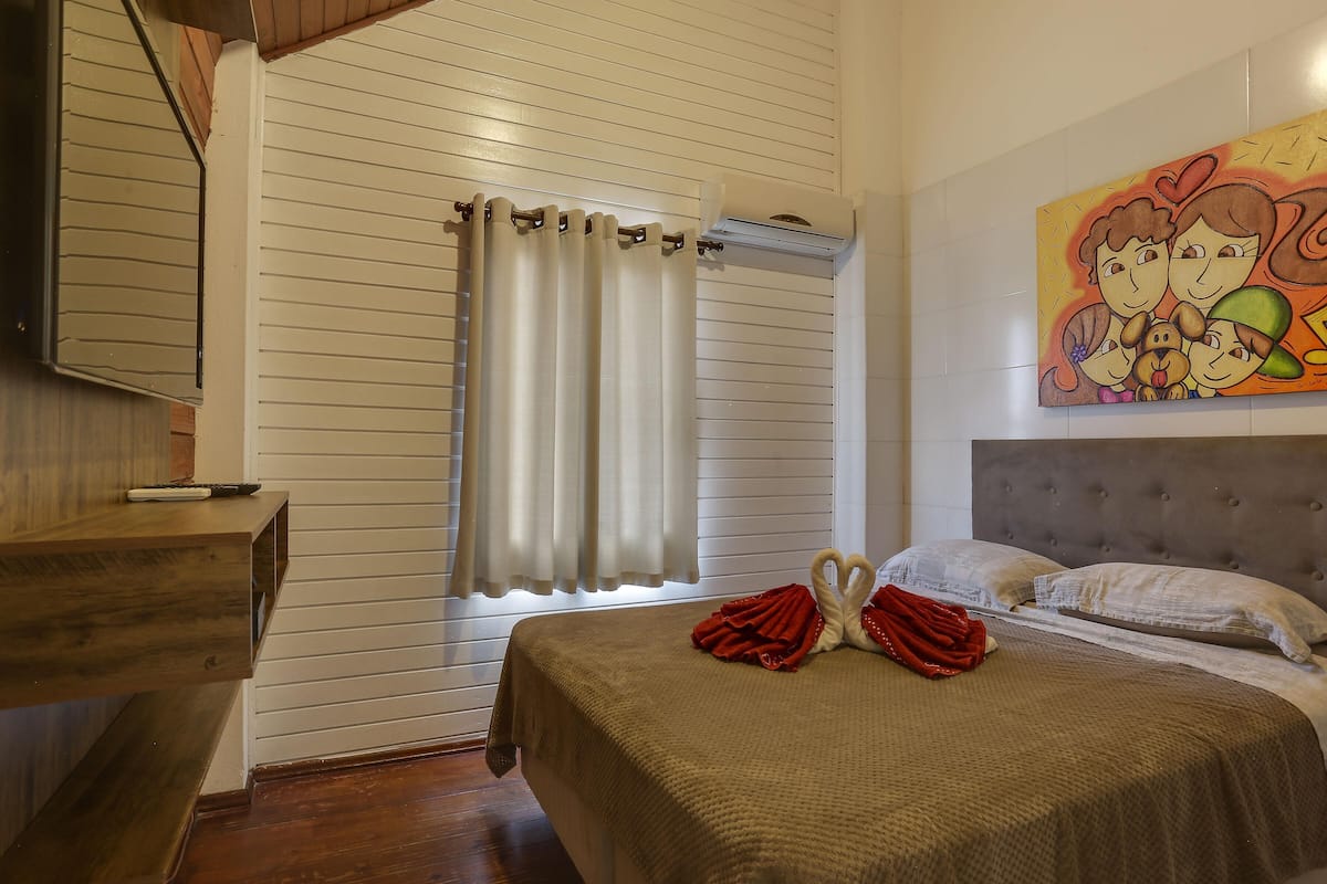 Une chambre à coucher avec un lit, une fenêtre avec des rideaux, un tableau au mur et un escalier en bois.