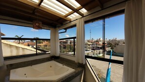 A bathroom with a large bathtub, a window with a view of a cityscape, and a ceiling with wooden beams. - Pousada Recanto do Aconchego (Florianópolis)