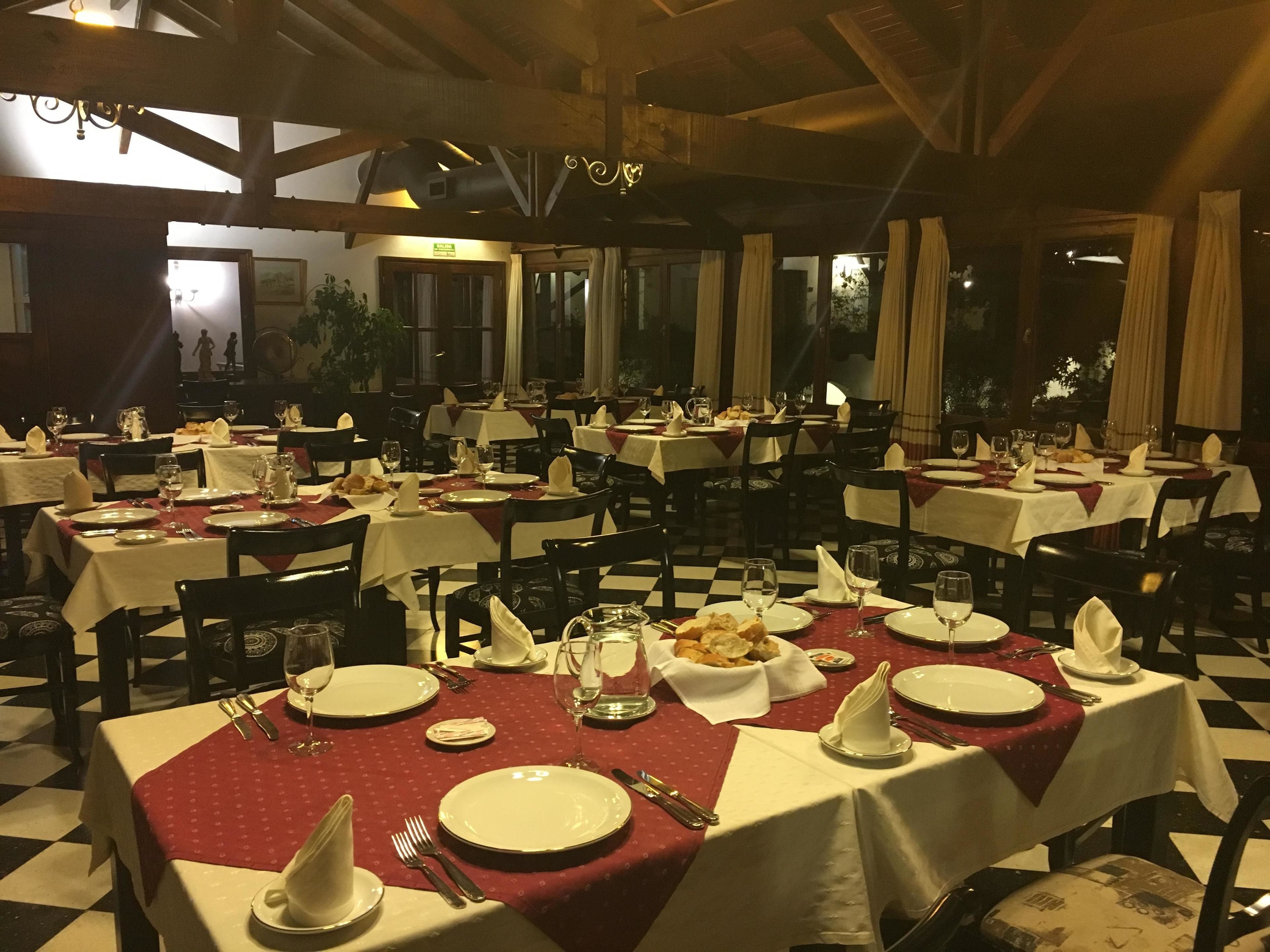 Un restaurante con varias mesas dispuestas para comer, con piso a cuadros y vigas de madera en el techo.