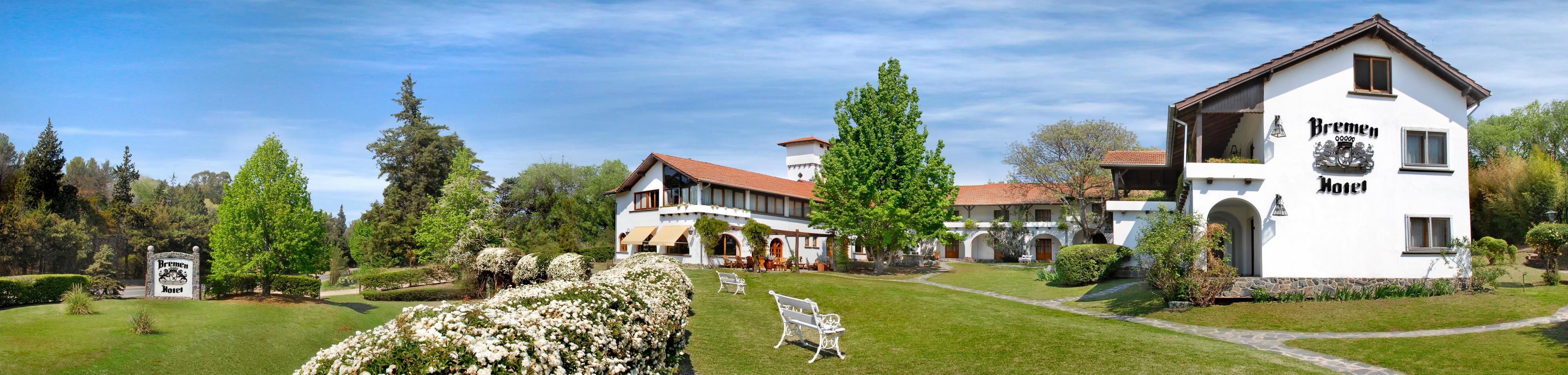 A large, white hotel with a traditional European architectural style, featuring a prominent entrance and a well-maintained garden with benches and a pathway.