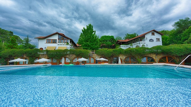 A swimming pool with a tiled floor, surrounded by buildings with arched windows and a cloudy sky. - Bremen Hotel & Spa (Villa General Belgrano)