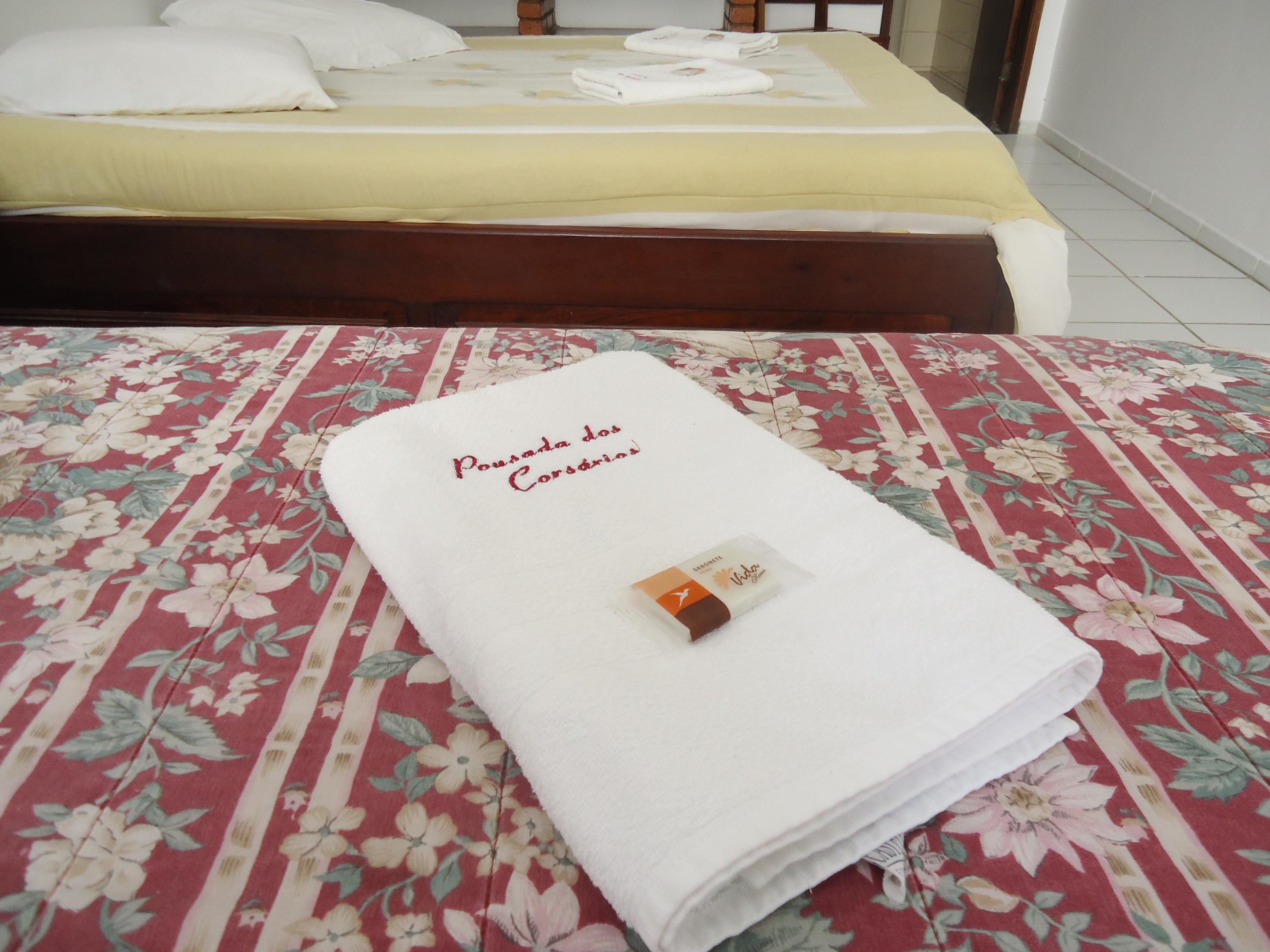A neatly made bed with a floral-patterned bedspread and a folded white towel with text on it.