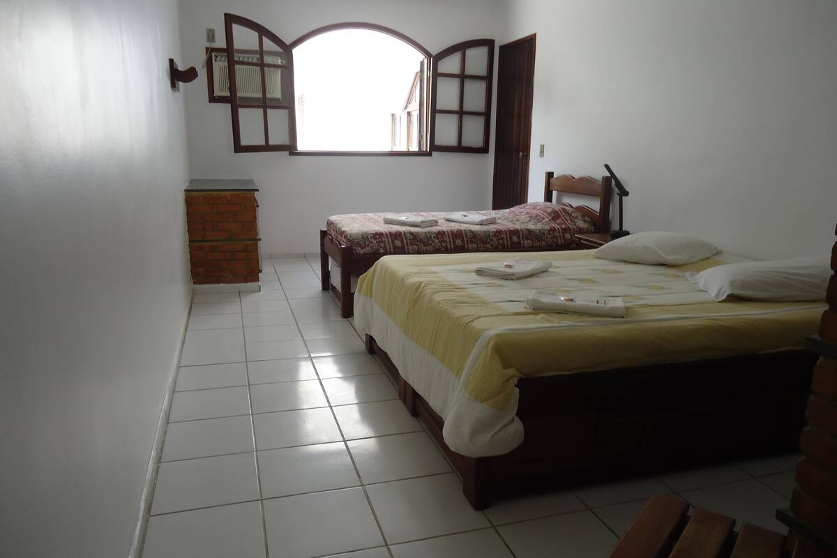 A bedroom with two beds, a wooden bench, a radiator, and a window with an open door.