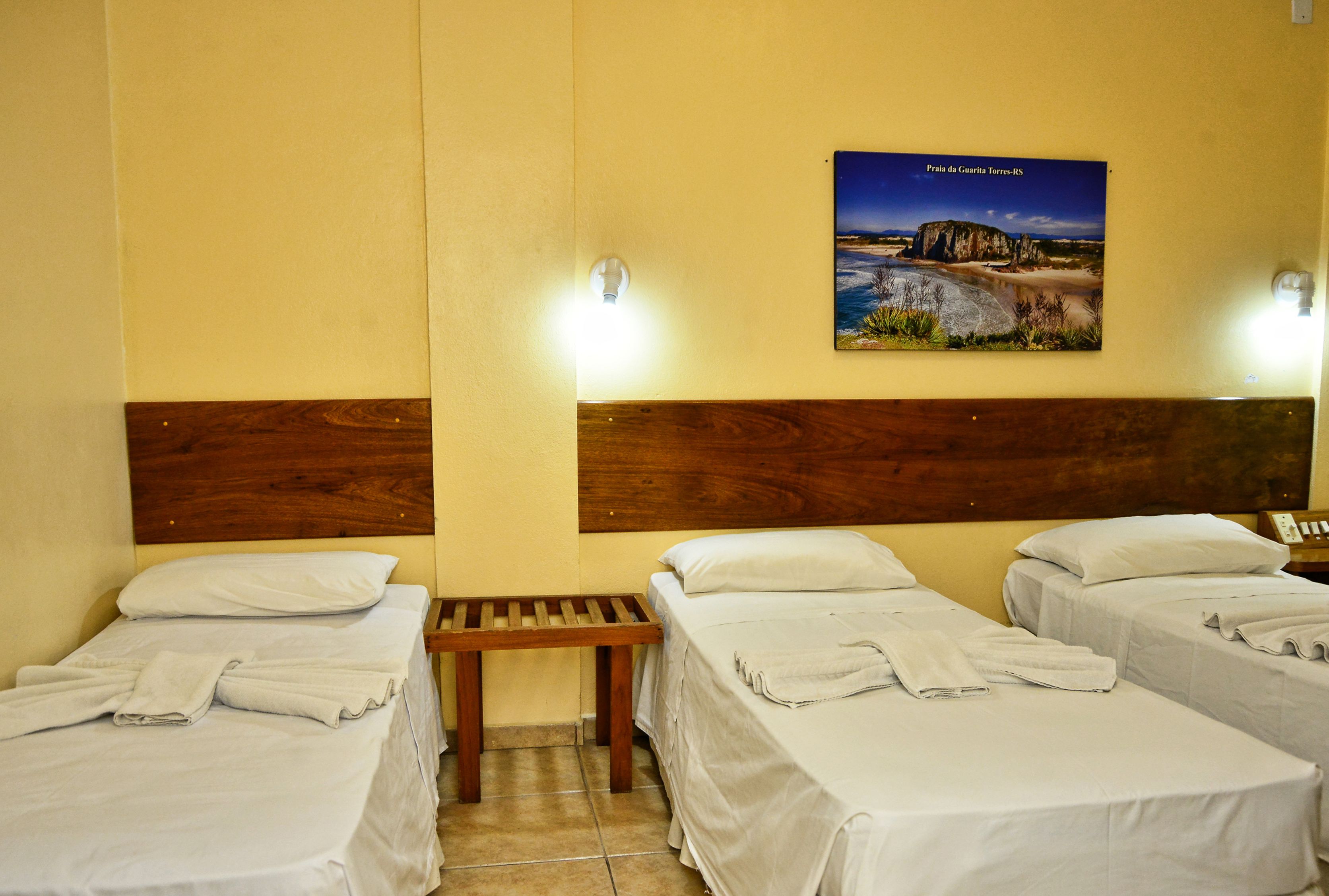 Habitació d'hotel amb dos llits individuals, un capçal de llit de fusta, un petit banc i un cartell a la paret.