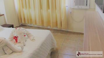 Habitación de hotel con cama, un peluche, cortinas, unidad de aire acondicionado y piso de baldosas.