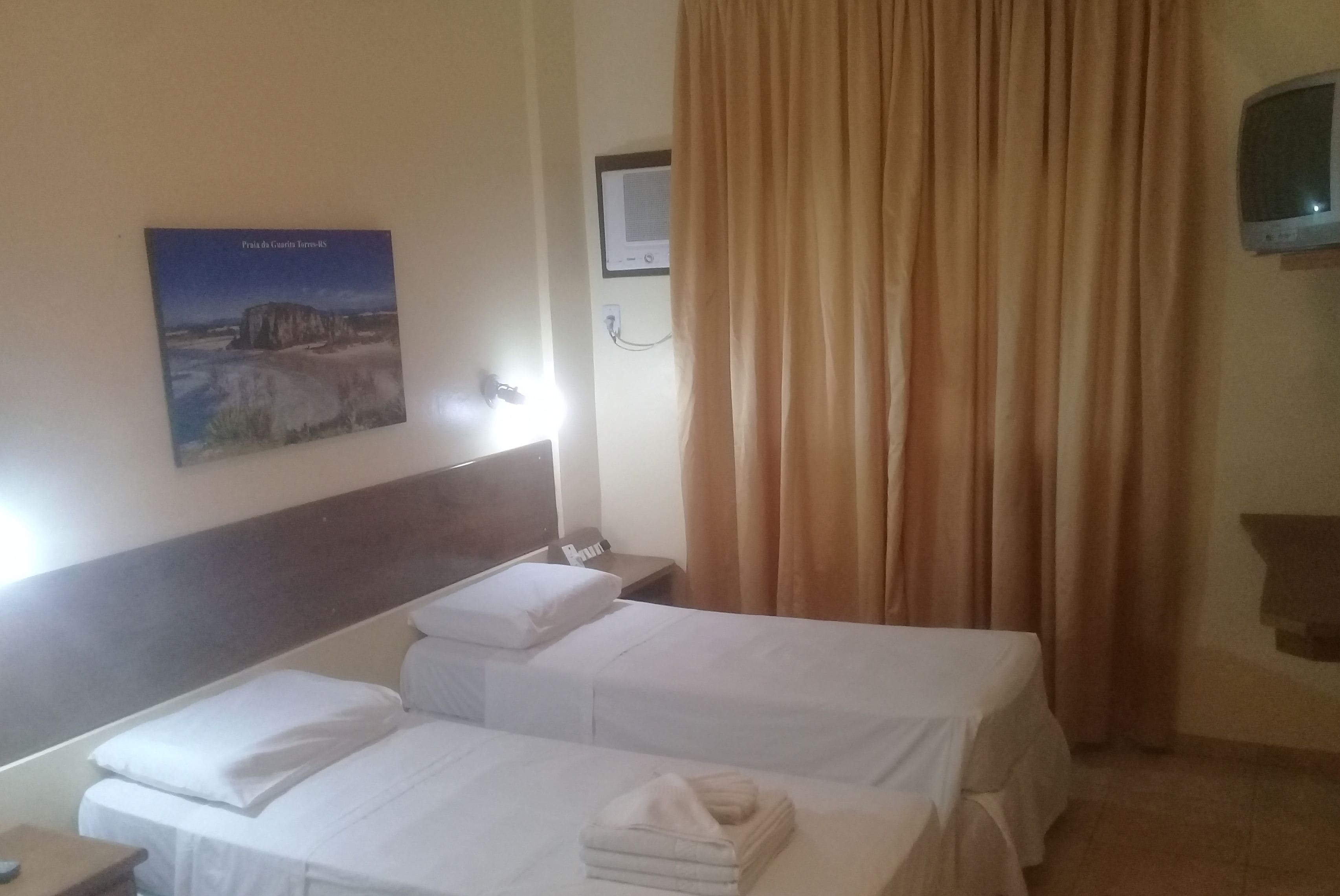 Ein Hotelzimmer mit zwei Einzelbetten, einem an der Wand befestigten Fernseher und einem Landschaftsbild.