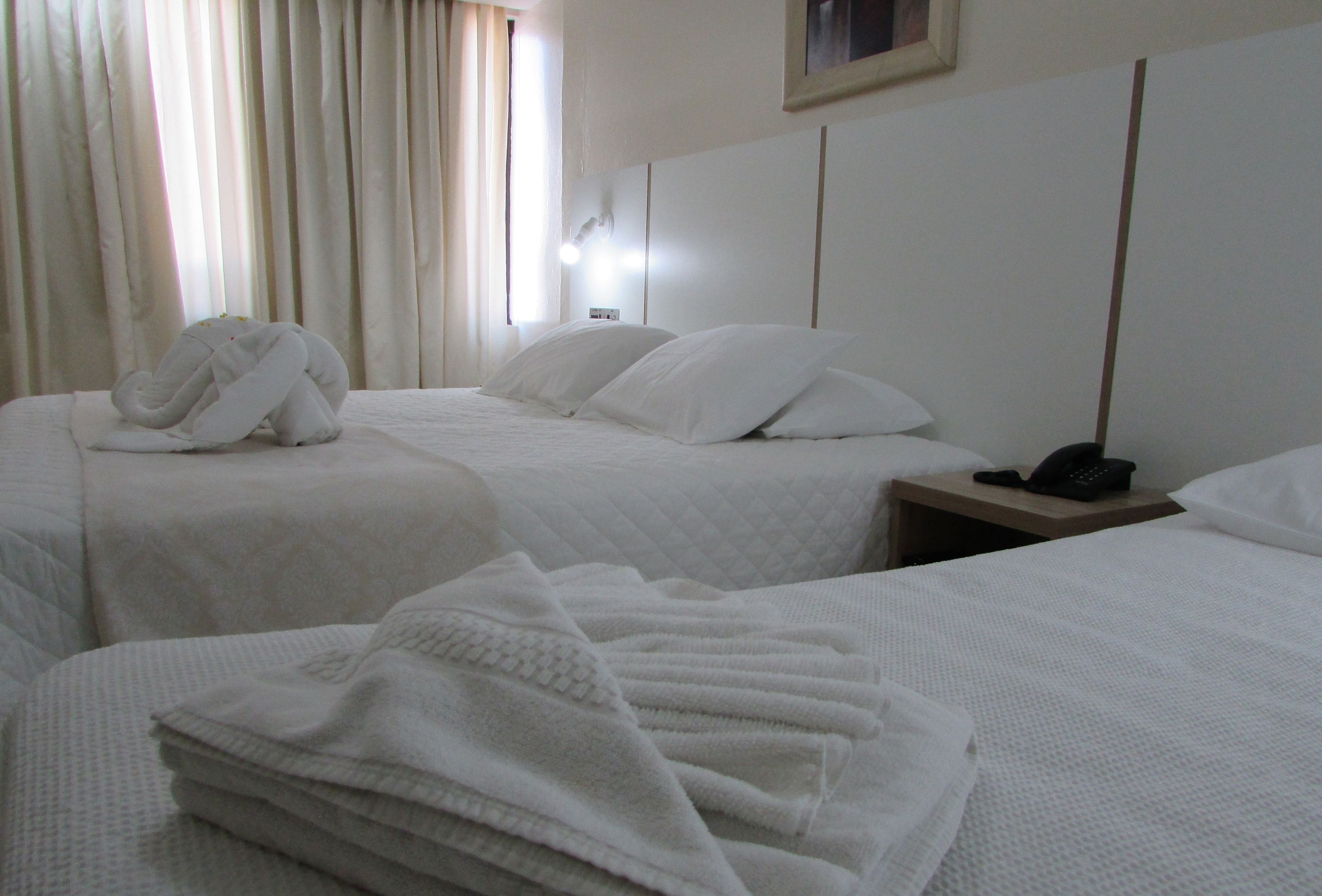 Habitación de hotel con dos camas, una mesita de noche con teléfono y una ventana con cortinas.