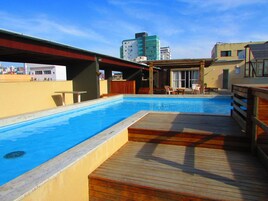 Una piscina en la azotea con cubierta de madera, una zona de estar cubierta y vistas de los edificios circundantes.