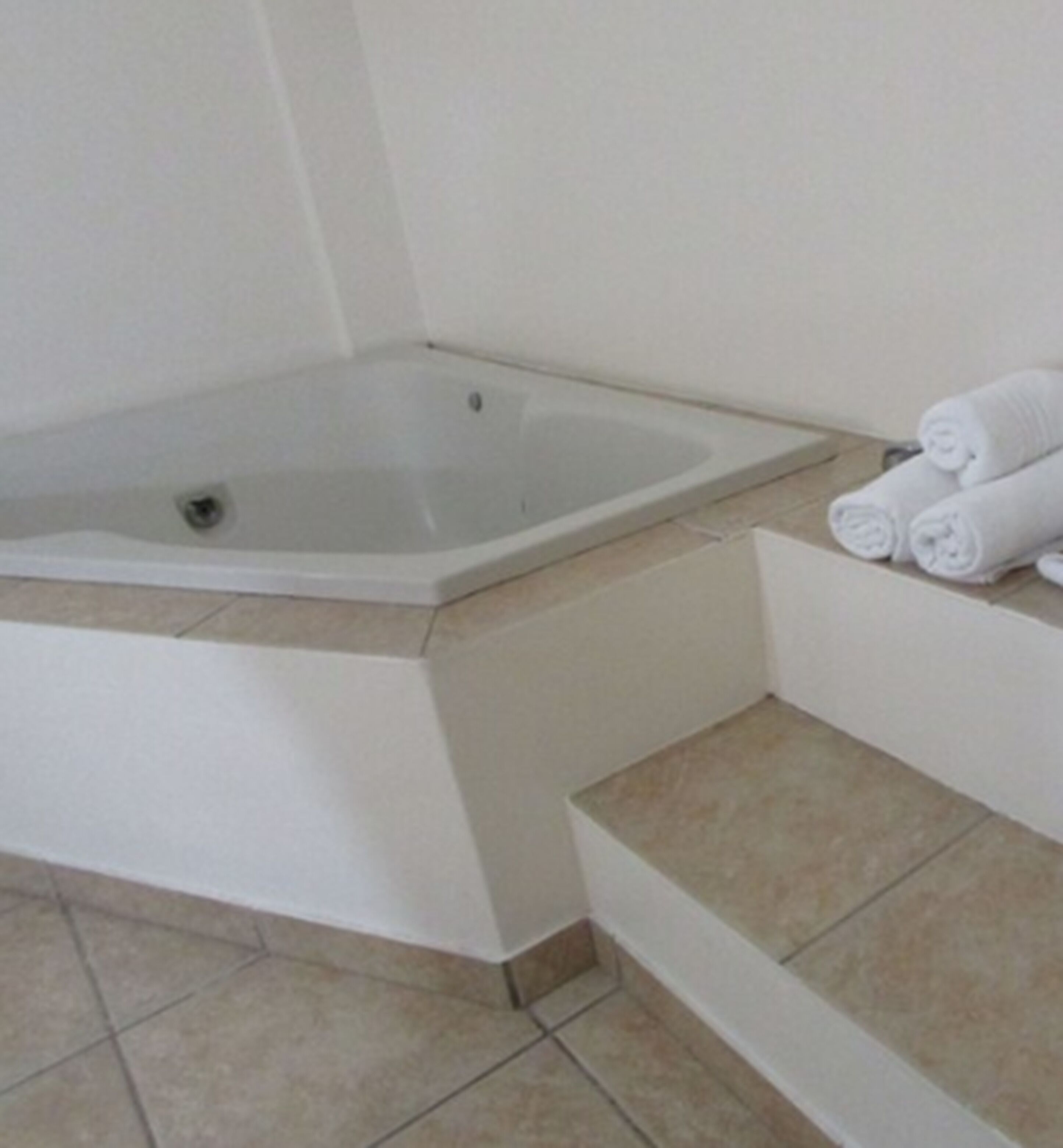 A bathroom with a bathtub, a toilet, and a sink. There are towels stacked on a ledge.