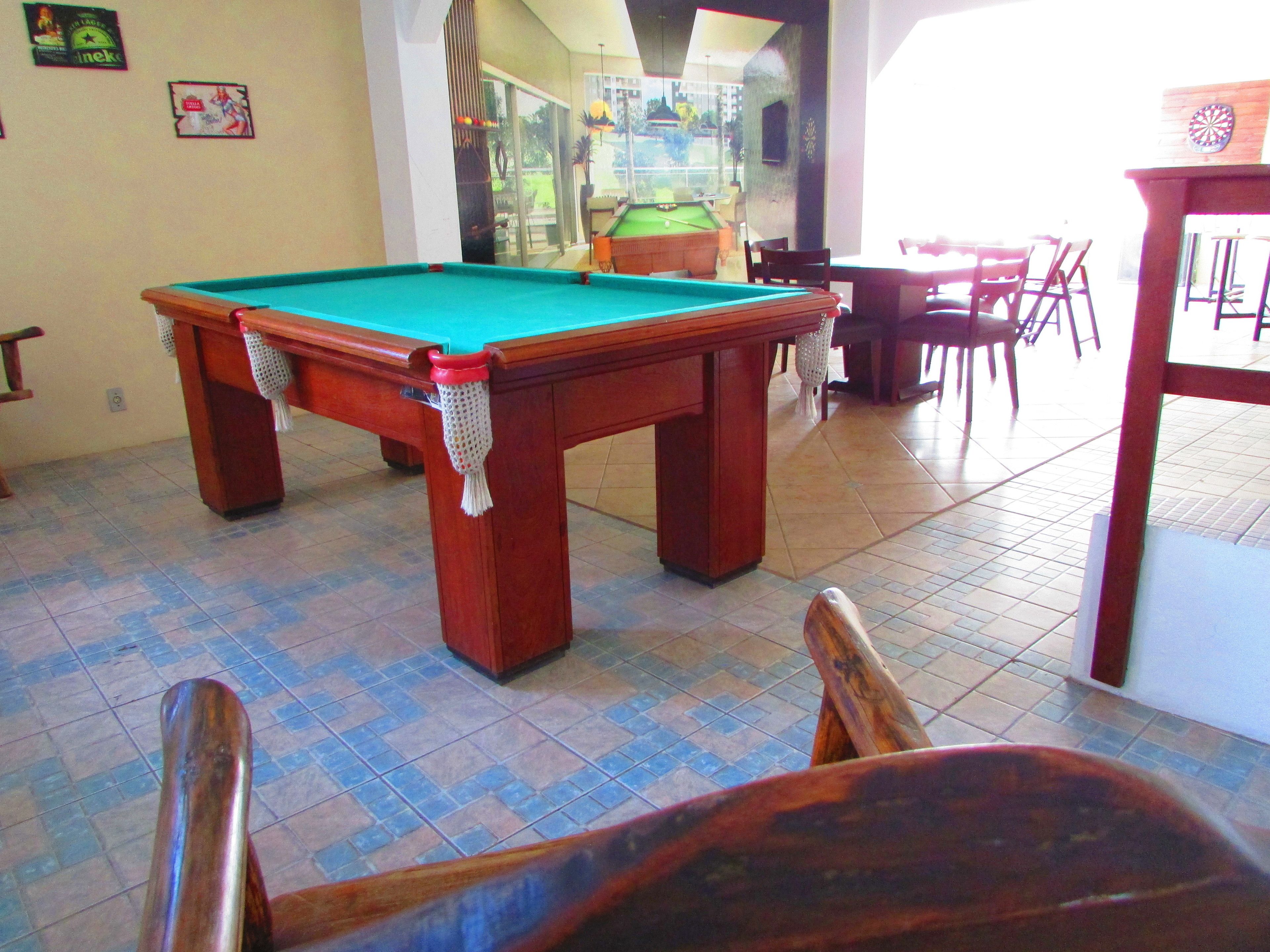 Una mesa de billar con superficie de fieltro verde, rodeada de sillas de madera y una mesa.