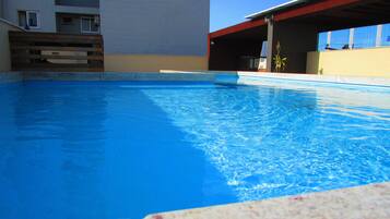 Guests can enjoy a refreshing swim in the pool surrounded by a concrete ledge and a wooden fence.