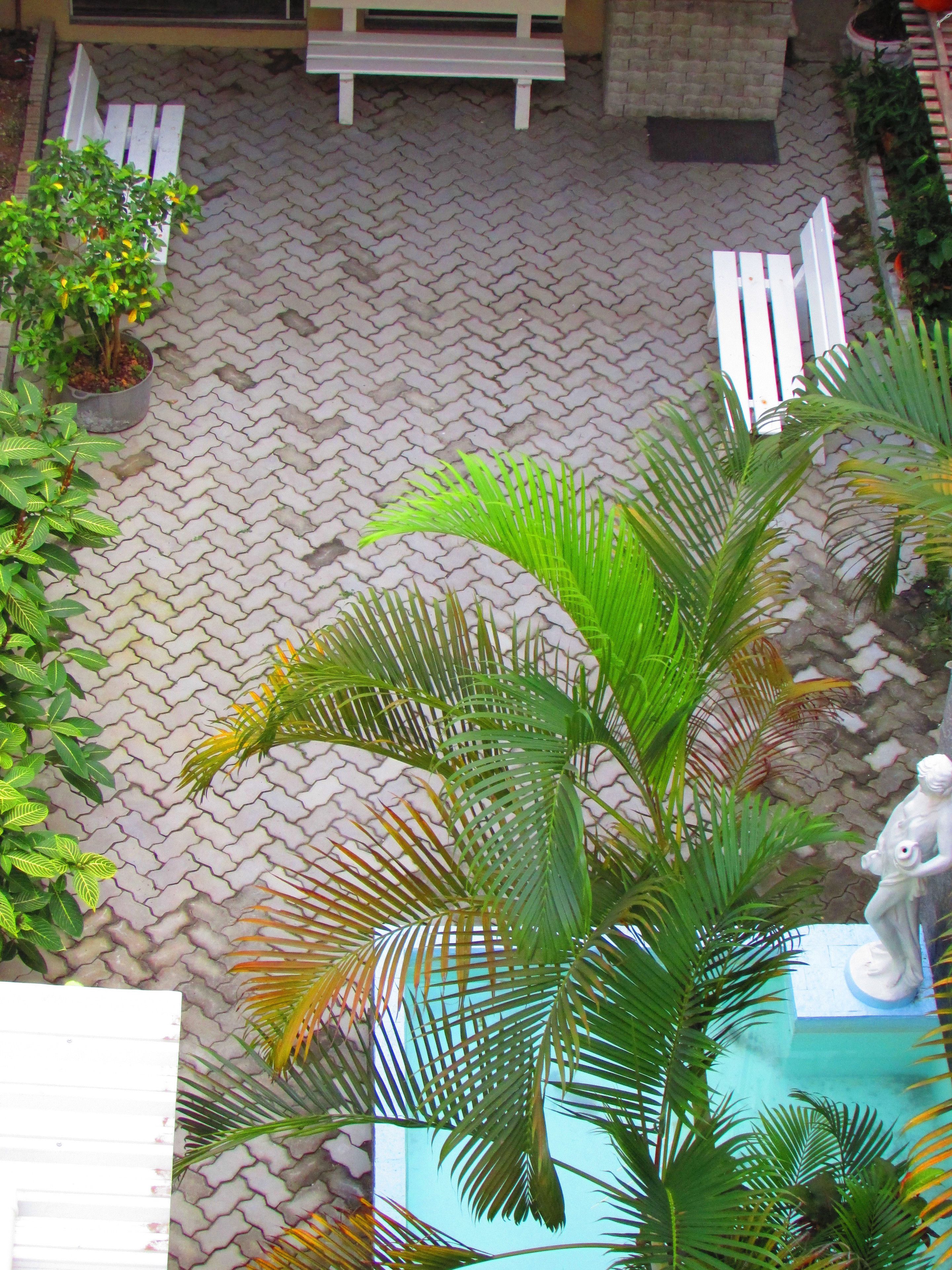 A courtyard with a patterned brick floor, potted plants, and a white bench.