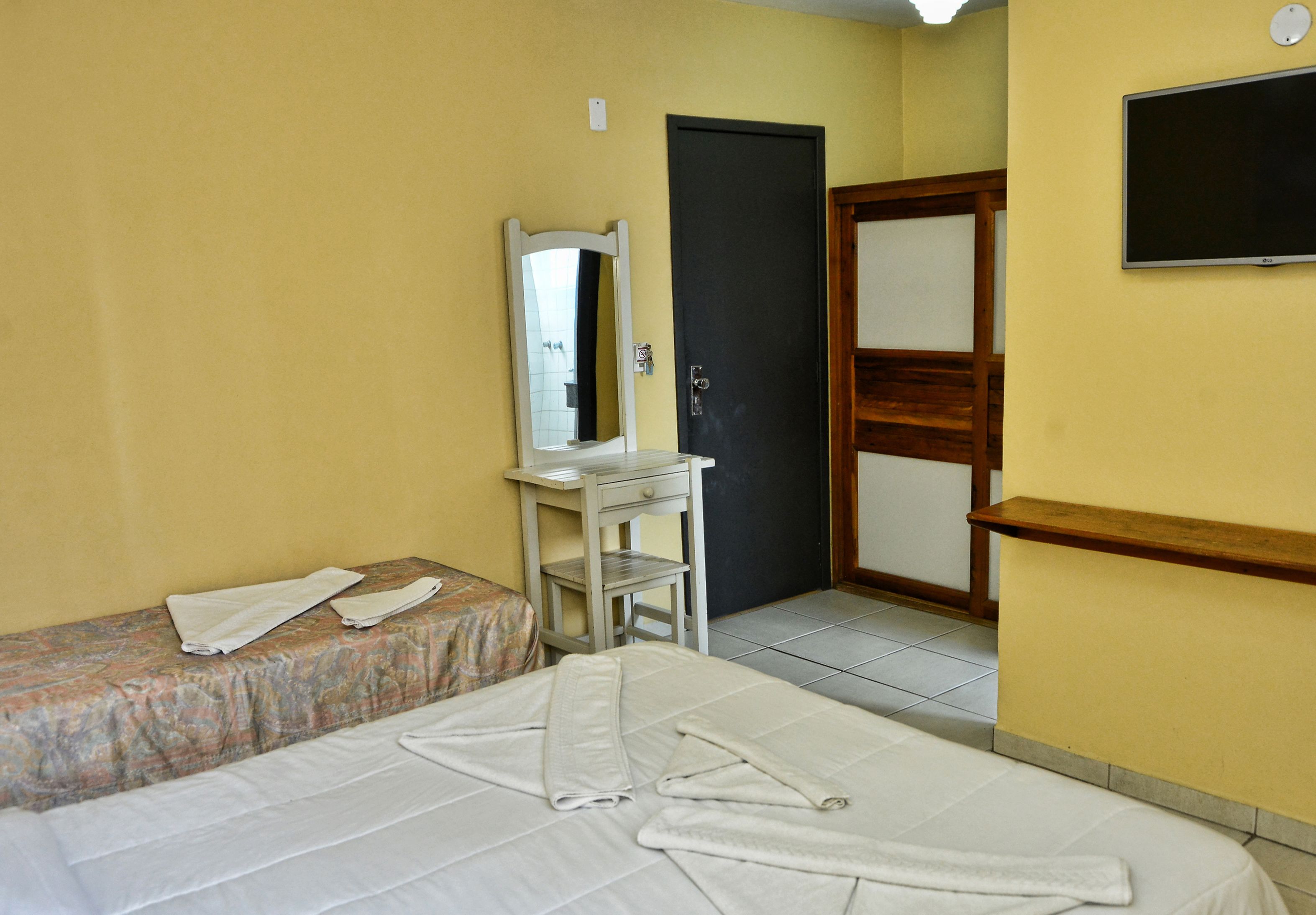 Habitación de hotel con cama, un escritorio pequeño con espejo, una puerta y un televisor montado en la pared.