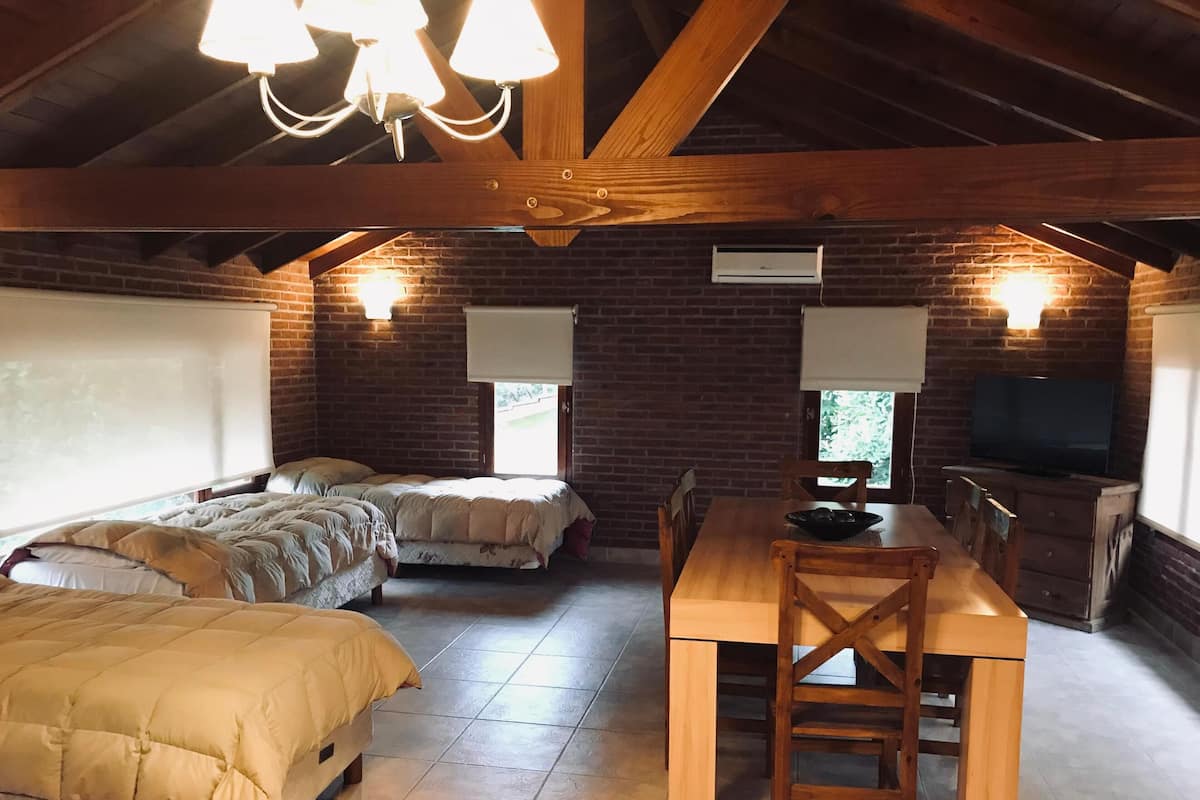 A cozy room with a wooden ceiling, a brick wall, a bed, a dining table, and a TV.