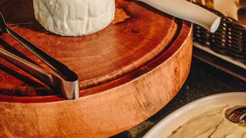 A cheese wheel on a wooden board with a cheese knife, surrounded by various food items.