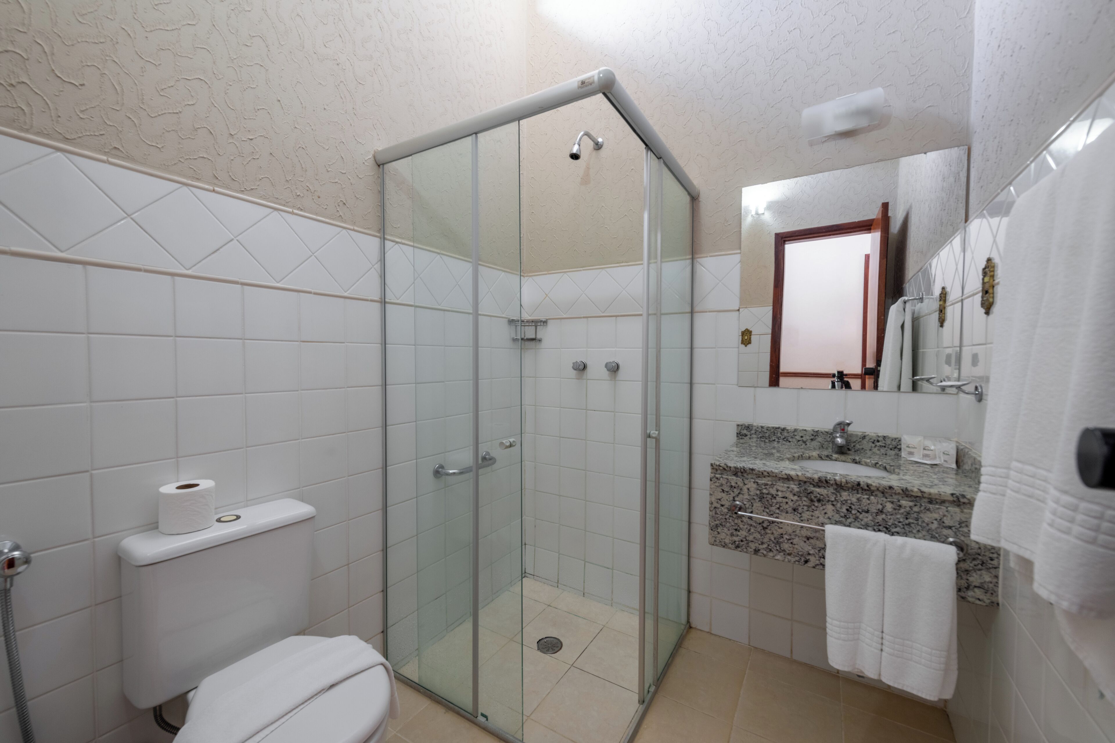 Un baño con ducha envuelta en vidrio, inodoro, lavamanos con encimera de granito y espejo con marco de madera.