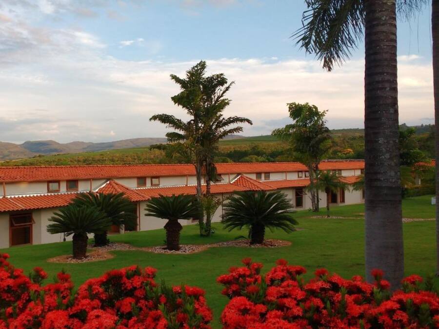 Um edifício com telhados de telhas vermelhas e paredes brancas, rodeado por relvados verdes e flores vermelhas.