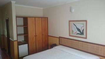 Quarto com cama, guarda-roupa, pequena escrivaninha e um quadro na parede.