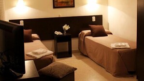 A hotel room with two single beds, a small table with a vase, and a nightstand. - Hotel Marconi (Resistencia)