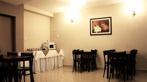 A dining area with a table set for four, a microwave, and a framed picture on the wall. - Hotel Marconi (Resistencia)