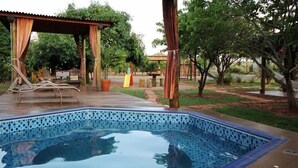 A swimming pool with a tiled edge, surrounded by a wooden deck and a covered seating area with chairs. - Hotel Flamboyant (Olímpia)