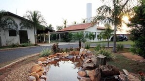A pond with a stone border, surrounded by rocks and plants, with a house in the background. - Hotel Flamboyant (Olímpia)