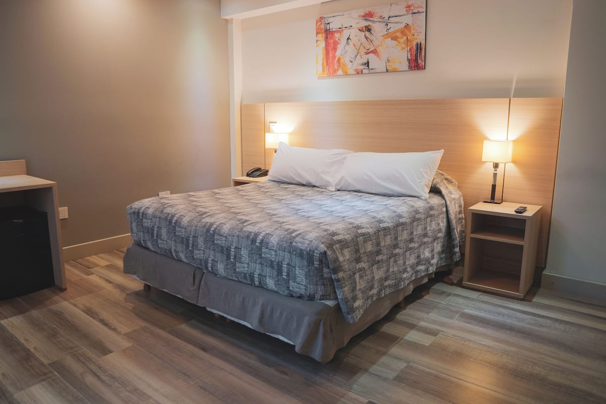 Una camera d'albergo ordinata con un letto grande, lampade sui comodini, un tavolino e un quadro appeso al muro.