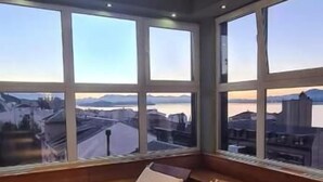 A room with two wooden beds and large windows offering a view of a cityscape and water.