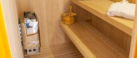 Un sauna con paredes y bancos de madera, toallas sobre los bancos y un cubo de madera.