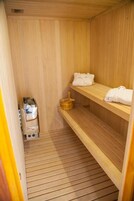 Un sauna con paredes y bancos de madera, toallas sobre los bancos y un cubo de madera.