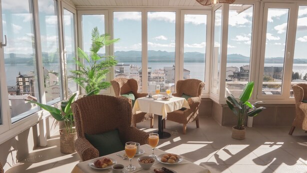 A sunlit dining area with wicker furniture, a table set with breakfast, and a view of the city and water.