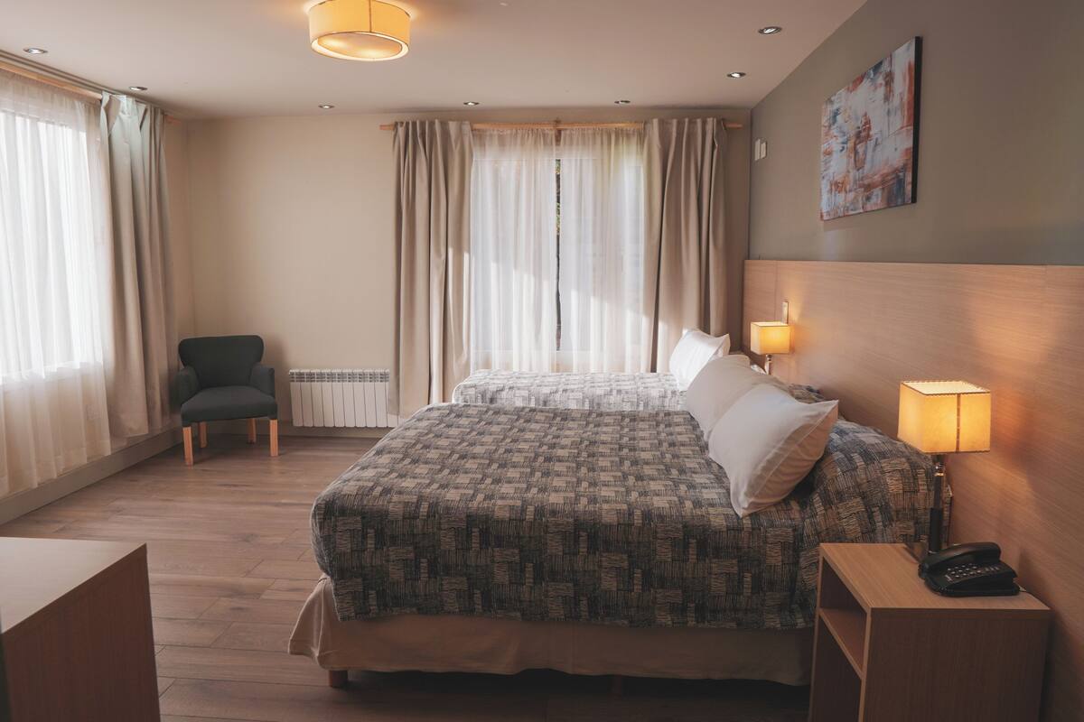 Una camera d'albergo con un letto grande, una poltrona, un comodino con una lampada e un quadro appeso al muro.