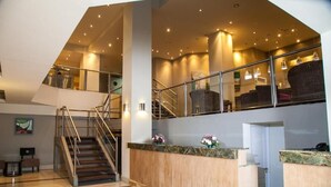 A spacious lobby with a central staircase, a reception desk, and seating areas.