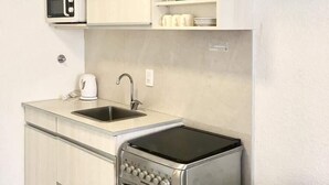 Una cocina compacta con microondas integrado, tetera, lavabo y estufa de acero inoxidable.