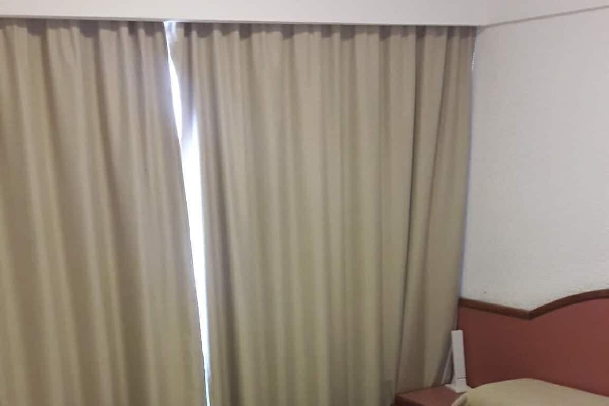 Una habitación de hotel con cama, cortinas, mesita de noche y cabecera roja.
