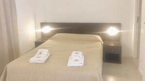 Una habitación de hotel con una cama, dos mesitas de noche y dos toallas dobladas sobre la cama.