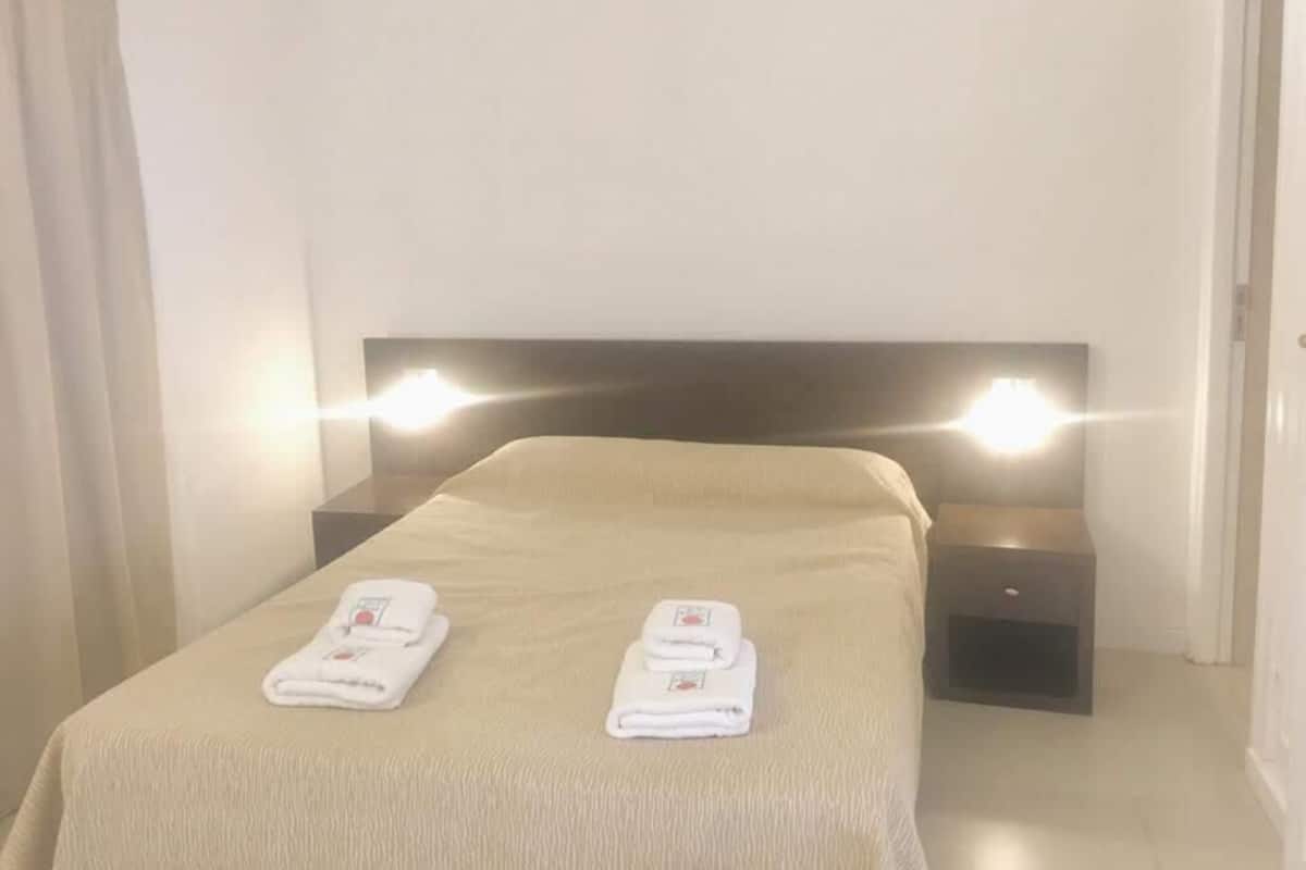Una habitación de hotel con una cama, dos mesitas de noche y dos toallas dobladas sobre la cama.