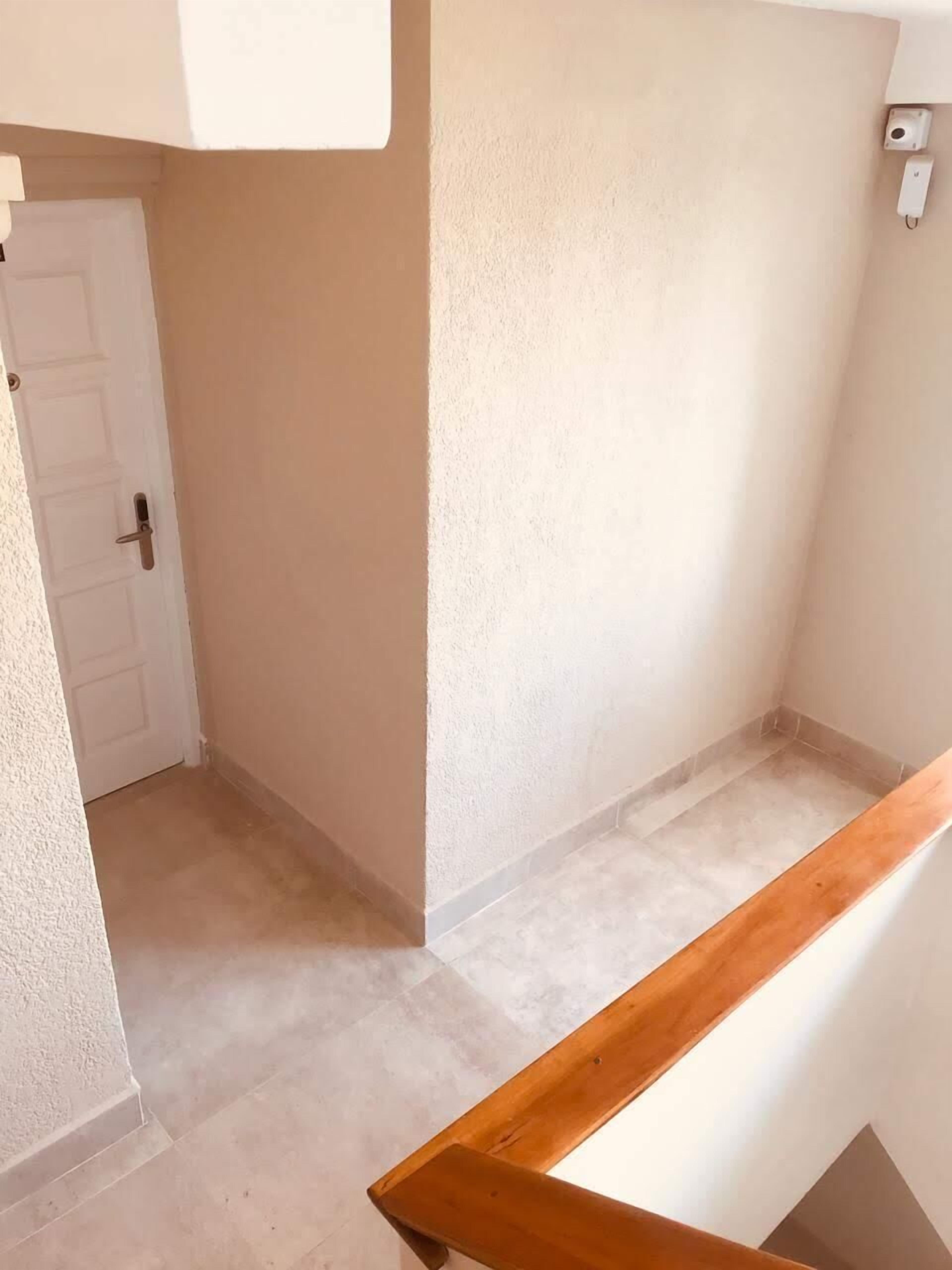 Un pasillo estrecho con una puerta y una pared blancos, y una barandilla de madera.