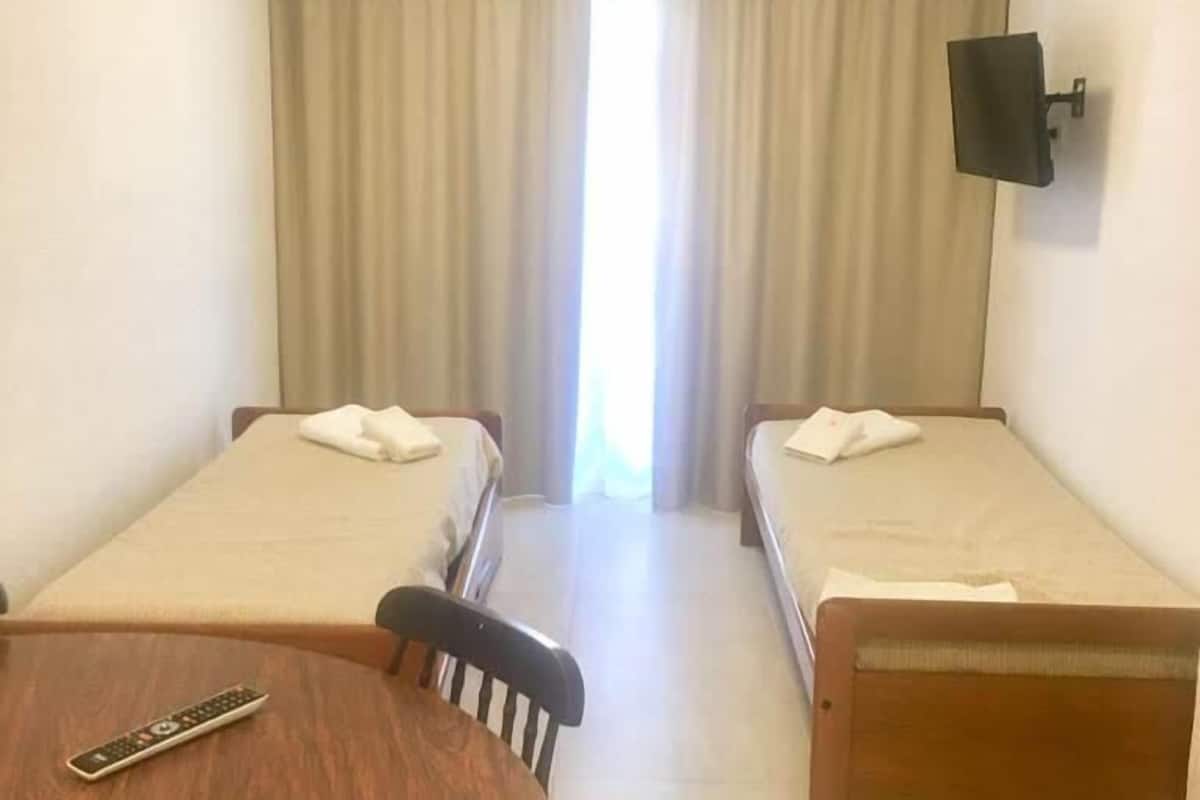 Habitación de hotel con dos camas individuales, una mesa redonda de madera, una silla y un televisor montado en la pared.