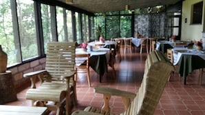 A covered outdoor dining area with wooden benches and tables, surrounded by large windows. - Hotel Panacam Lodge (Santa Cruz de Yojoa)