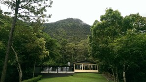 A small, single-story building with a sloped roof, surrounded by lush greenery and a mountain in the background. - Hotel Panacam Lodge (Santa Cruz de Yojoa)