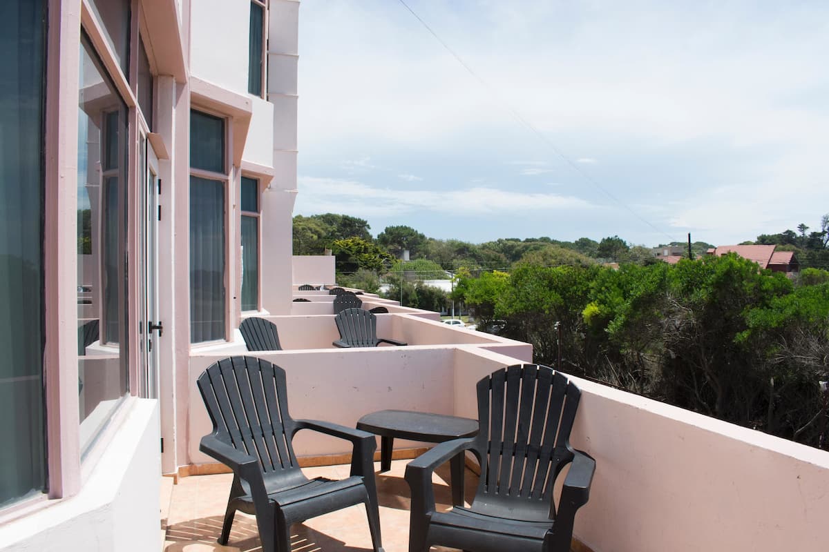A balcony with two chairs and a table, overlooking a residential area with trees and houses.