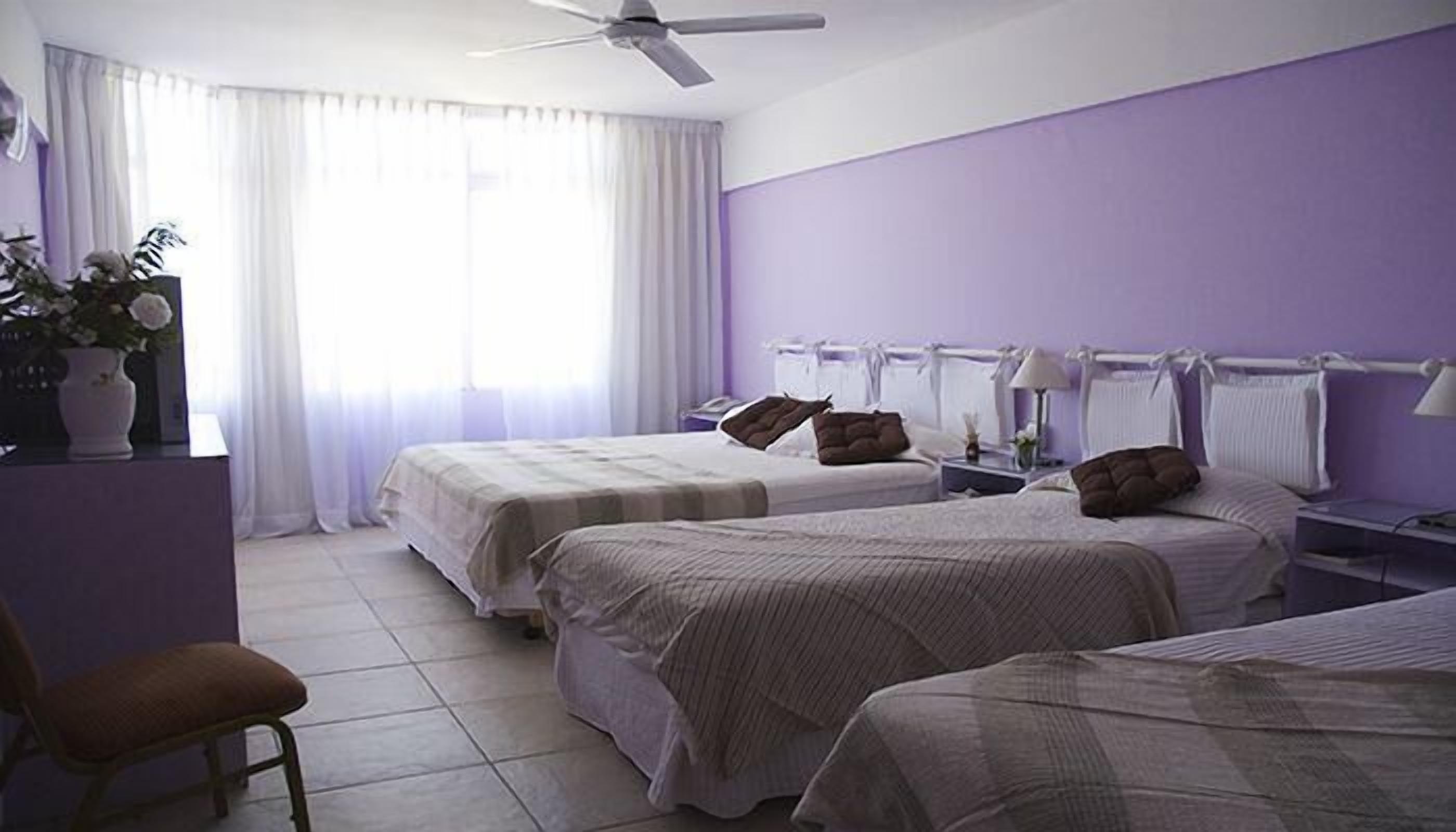 A hotel room with two beds, a ceiling fan, a chair, and a bedside table with a lamp.
