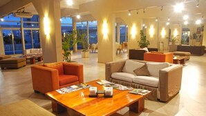 A spacious lobby with a wooden coffee table, sofas, and chairs. Large windows provide natural light and views of the outdoors.