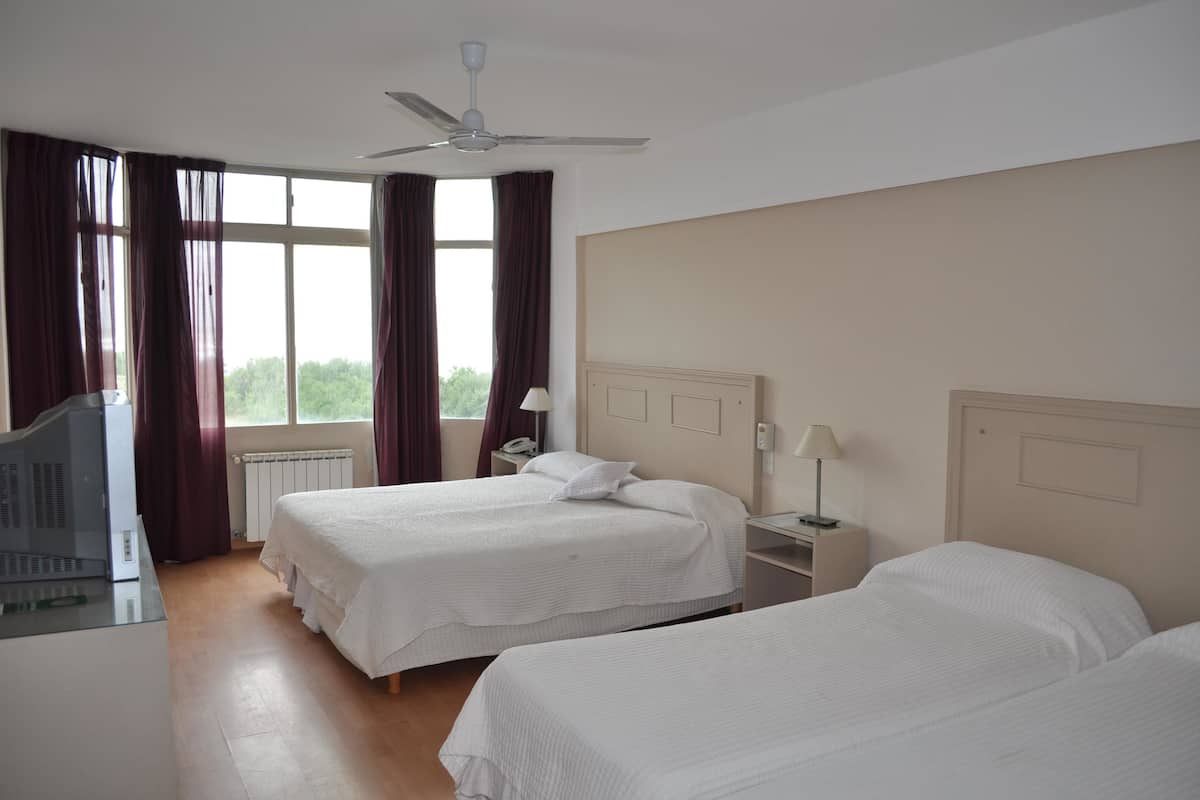 A hotel room with two beds, a ceiling fan, a desk with a computer, and a window with curtains.