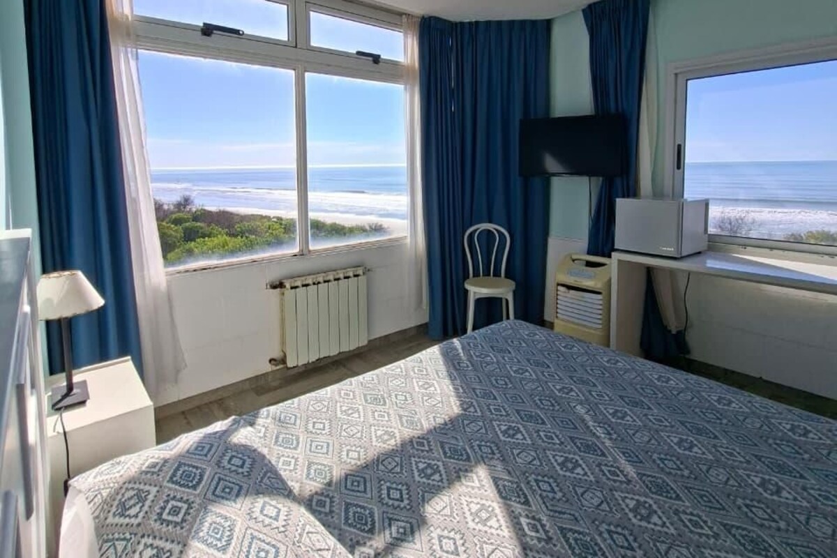 Una camera d'albergo con un letto, una ventola a soffitto, una TV e vista sul mare.