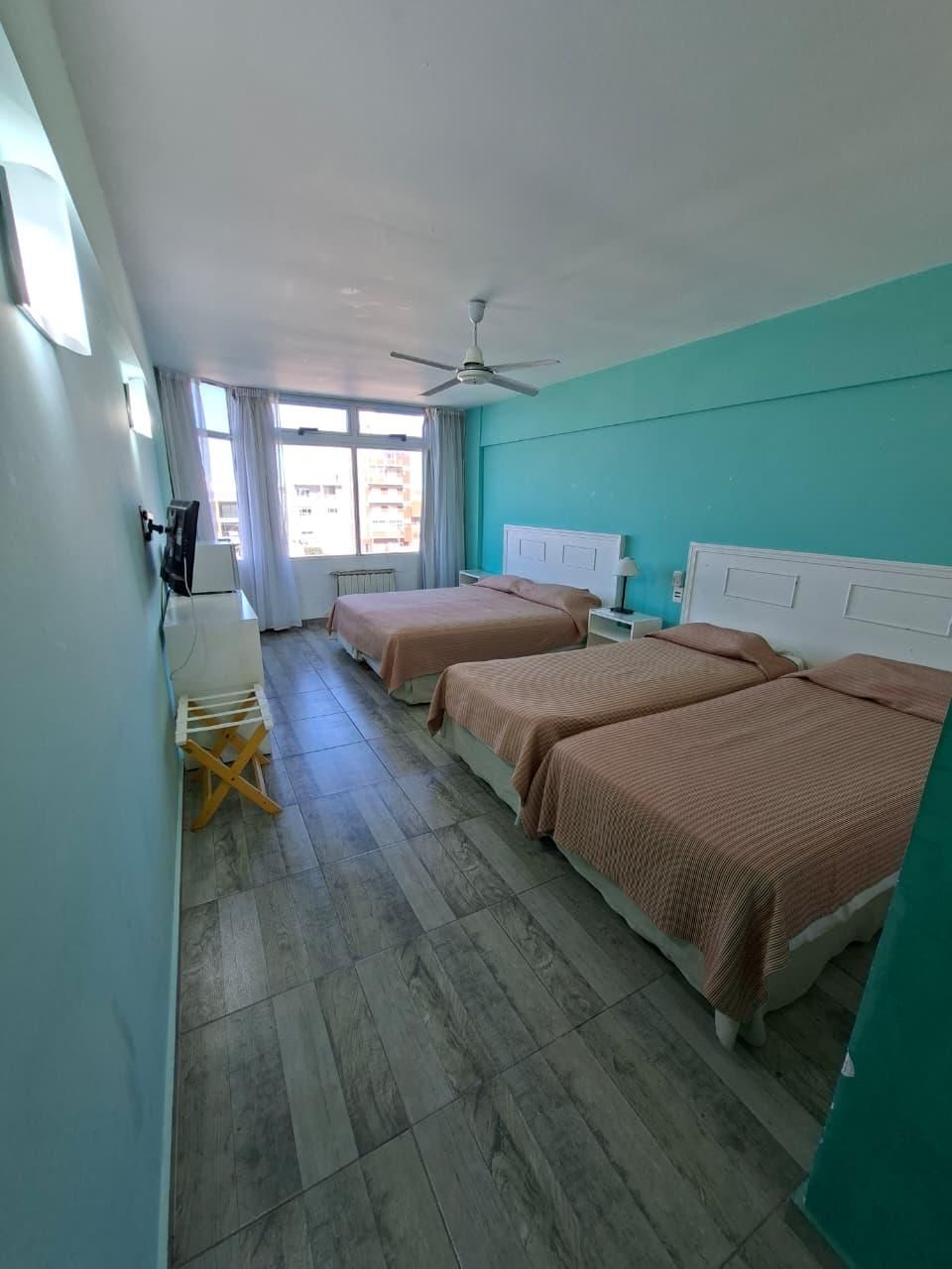A hotel room with two beds, a ceiling fan, a TV, and a window with curtains.