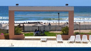 A pool area with lounge chairs and a view of the ocean.