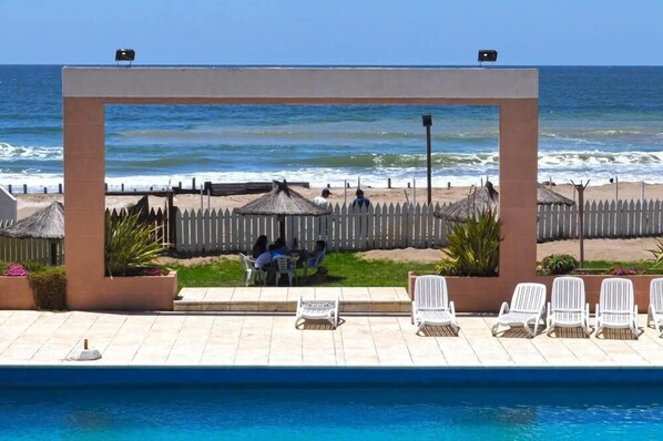 A pool area with lounge chairs and a view of the ocean.