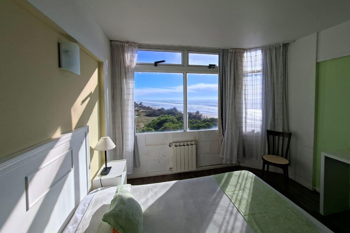 Una stanza con un letto, una sedia, una finestra vista e un termosifone.